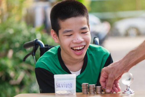 Child in wheel chair with stacks of coins learning to save money